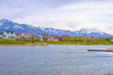 Scenic view of a lake with homes near the shore against mountain and cloudy skyの写真素材