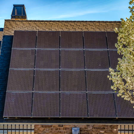 Square frame Solar panel on the dark pitched roof of a house against blue sky on a sunny day