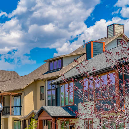 Square Blue sky with puffy clouds over row of lovely houses and trees on a sunny dayの写真素材