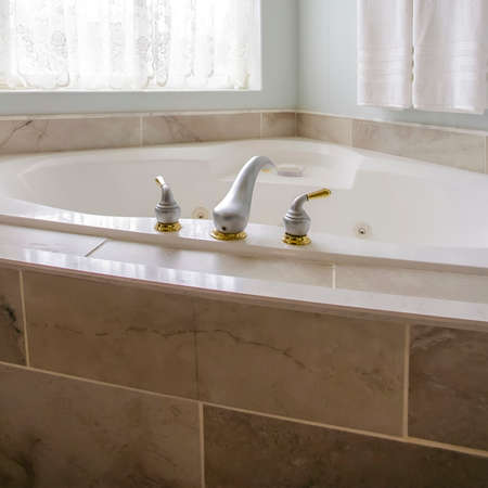 Square Built in bathtub at the corner of a bathroom with a large arched window