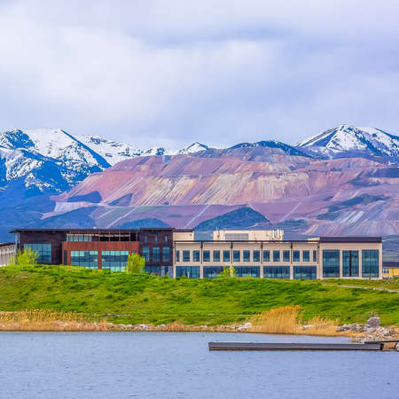 Square Buildings and snowy mountain beyond the grassy shore of a lake on a cloudy day