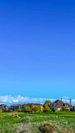 Vertical Vast grassy terrain with houses under blue sky and puffy clouds on a sunny dayの写真素材