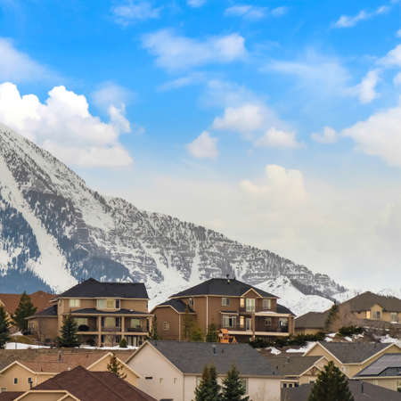 Square frame Exterior view of houses with pitched roofs against mountain and cloudy blue skyの写真素材