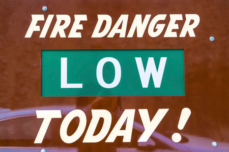 Close up view of a sign that reads Fire Danger Low Today. Reflection of a person and a car can be...