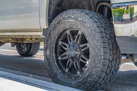 Black rubber wheel of a silver vehicle parked on the road on a sunny day