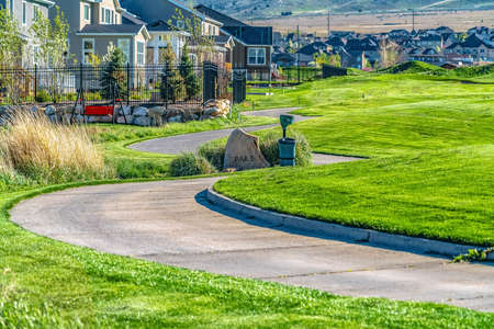 Narrow paved road that winds through vast grassy terrain viewed on a sunny day. Houses on the residential area in the valley can be seen in the distance.の写真素材