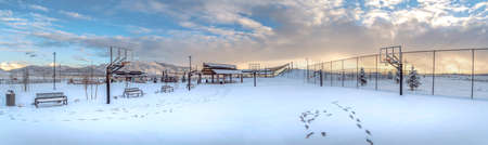 Panoramic view of a park and mountain covered with snow on a cloudy winter day. Basketball court,...