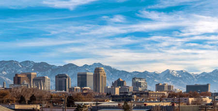 Building and skyscrapers on a city with snow covered mountain in the background. Blue sky with...