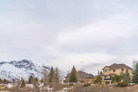 Homes with view of snow covered mountain and overcast sky in winter. Lush coniferous trees can be seen growing around the residences.の写真素材