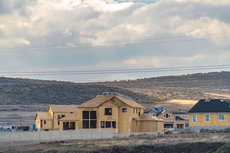 Homes under construction against a hill with bushes and road