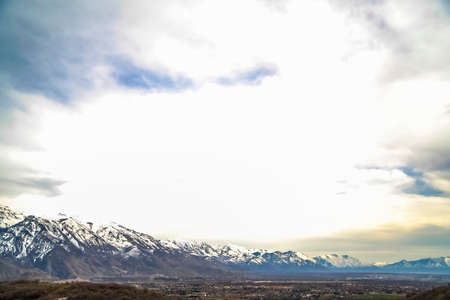 Blue sky filled with bright thick clouds over towering mountain and vast valley. The peaks of the...