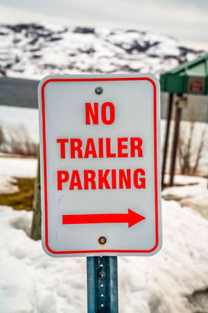 Close up of a white and red No Trailer Parking with arrow sign in winter. In the background is a...