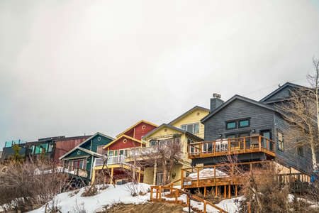 Facade of mountain homes with horizontal siding balconies and outdoor stairs. Gray cloudy sky and snow covered ground in winter can also be seen in this landscape.の写真素材