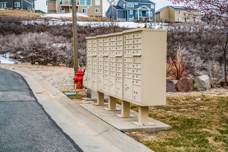White metal cluster mailboxes and red fire hydrant along a concrete road. Multi-storey homes and snow covered ground can be seen in the background.の写真素材