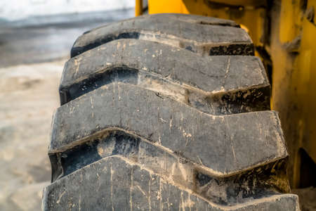 Thick black rubber tire of a yellow construction equipment viewed in winter. The dirty and heavy duty wheel has tread with diagonal design.の写真素材