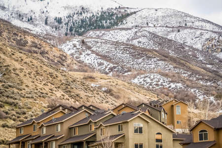 Exterior view of homes with snow topped mountain and cloudy sky background. The houses have pitched...