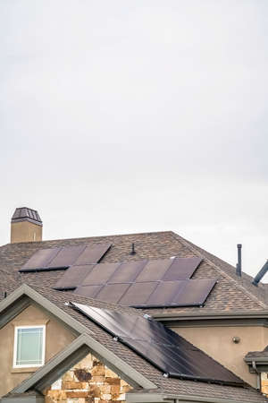 Solar panels on the dark pitched roof of a home with cloudy sky background. The exterior wall of this house is a combination of concrete and stone sections.の写真素材