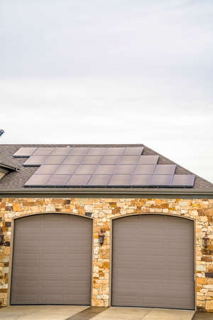 Solar panels installed on the garage roof of a home with cloudy sky background. Gray garage doors...