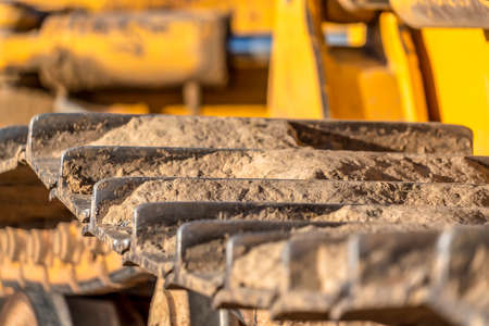 Metal grouser pad close up of a yellow construction vehicle on a sunny day. The track of the excavator is covered with dry brown soil.の写真素材