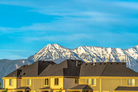 Homes with horizontal wall didings against snow peaked mountain and blue sky. Chimney pipes can be...