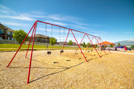Park with swings pavilion and slides in front of homes and lake on a sunny day. Distant snow capped mountain and blue sky can also be seen in this scenic landscape.の写真素材