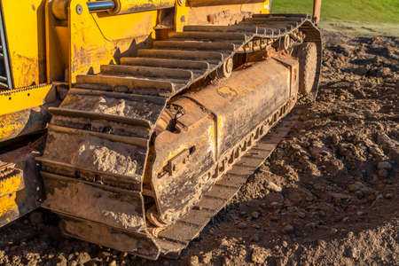 Dirty metal track pad of a yellow construction machinery on a sunny day. The track frame and rollers...