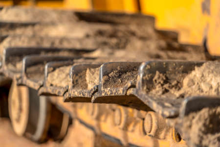 Close up of the metal grouser pad of a yellow contruction machine on a sunny day. The track of the excavator is covered with dry soil.の写真素材