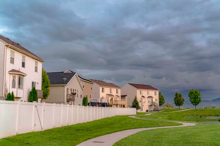 Home facade overlooking an expansive green field with a paved pathway and pond. A gray overcast sky can be seen over the landscape.の写真素材
