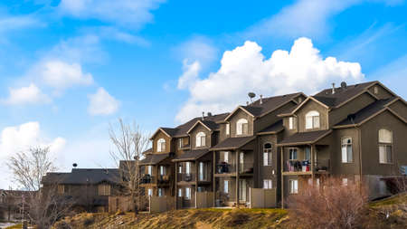 Panorama frame Houses with balconies and arched windows against blue sky with puffy clouds. Paved pathway on a grassy terrain can be seen in the foreground.の写真素材