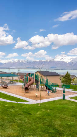 Vertical Playground and homes on a residential area with view of lake and snowy mountain. White flowering trees line the pathway under cloudy blue sky.の写真素材