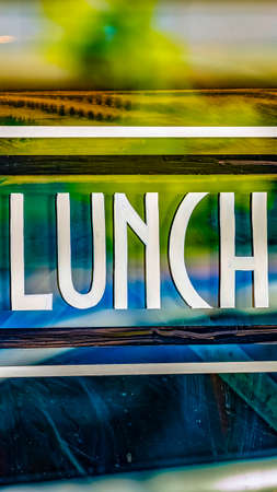 Vertical Close up view of a Lunch sign against the glass wall of a restaurant. The glossy glass surface reflects vehicles and buildings outdoor.の写真素材