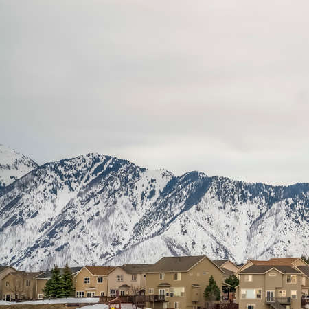 Square frame Striking snow capped mountain and multi storey houses under overcast sky. Coniferous...