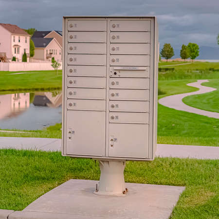 Square frame Cluster mailbox against pond and houses under sky with thick gray cloudsの写真素材