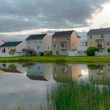 Square Family homes and bright cloudy sky reflected on the shiny neighborhood pondの写真素材