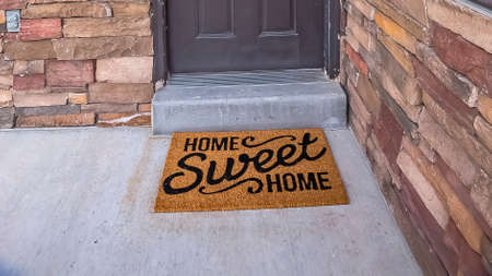Panorama White wreath hanging on gray front door of home with a doormat by the doorstep. The home has a combination of wood, concrete, and brick exterior wall.の写真素材