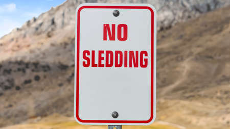 Panorama frame Close up of a No Sledding sign with a towering mountain in the background. Blue sky with bright clouds can be seen over the landscape on this sunny day.の写真素材