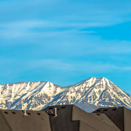 Square Homes with horizontal wall didings against snow peaked mountain and blue sky. Chimney pipes...