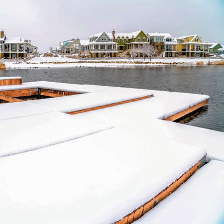 Square frame Adirondack wooden chairs on a deck overlooking lake and houses in winter. The seats and...