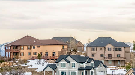 Panorama Multi storey homes built on a snow covered slope against cloudy sky in winter. View of a snow capped mountain can be seen in the background.の写真素材