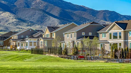 Panorama Multi storey homes with towering mountain and blue sky background on a sunny day. Vast terrain covered with lush green grasses can be seen in front of the houses.の写真素材