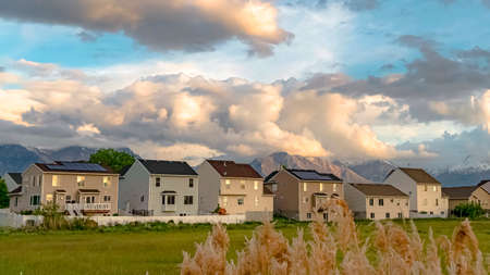 Panorama Tall brown grasses with stylish homes and snow capped mountain in the background. Blue sky with thick gray clouds can be seen over the neighborhood.の写真素材