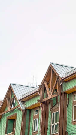 Vertical frame Exterior of the upper storey of homes with balconies and green horizontal siding. A chimney pipe on the pitched roof can be seen against the cloudy sky.の写真素材