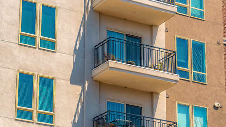 Panorama Exterior of a residential building with small balconies viewed on a sunny day. White blinds...