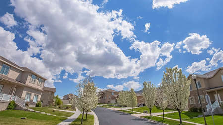 Panorama frame Paved road and homes on a neighborhood under cloudy blue sky on a sunny day. Lawns...