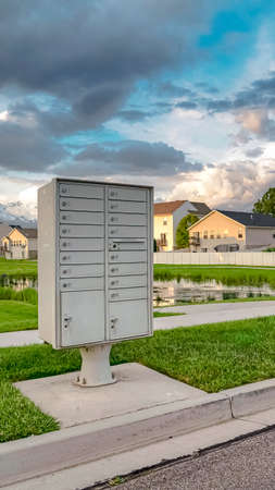 Vertical Mailbox on the side of the road with pond grassy terrain and homes background. Snow capped...