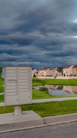 Vertical Sky filled with gray clouds over homes and pond amid a vast grassy terrain. White metal...