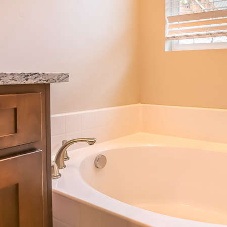Square frame Bathroom interior with oval bathtub against white wall and window with blinds. The...