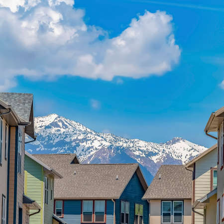 Square frame Road amid multi storey homes under cloudy blue sky on a sunny day. A mountain topped...