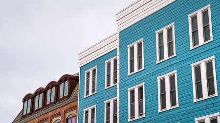 Panorama Residential building with blue exterior wall and vertical sliding windows. Over the building is a cloudy sky while a string of colorful lights is in front.の写真素材