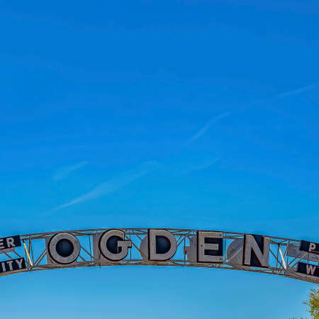 Square Welcome arch at the city of Ogden in Utah against lush treetops and blue sky. Spire of a...